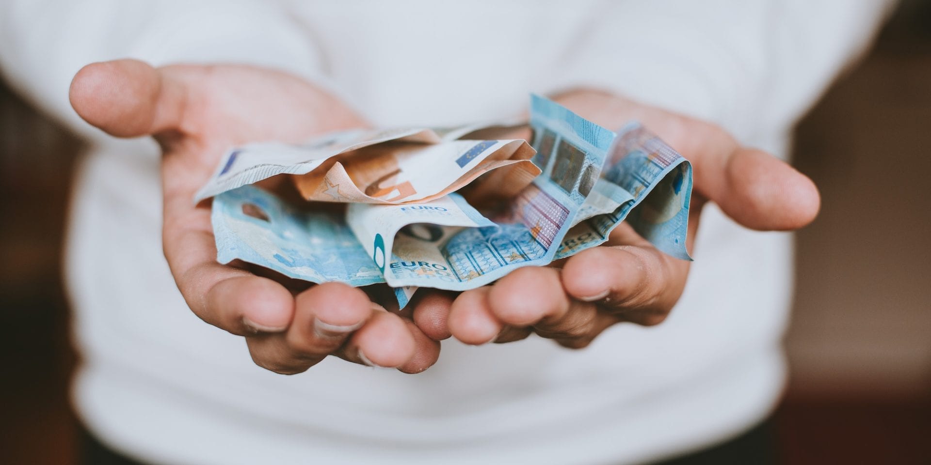 Zwei Hände halten mehrere zerknitterte Euro-Scheine.